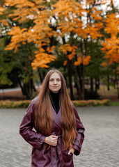 Woman with long hair in maroon coat standing in autumn park setting