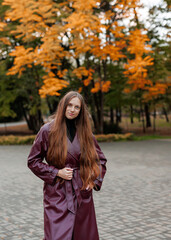 Woman in maroon coat poses outdoors among autumn trees and pavement