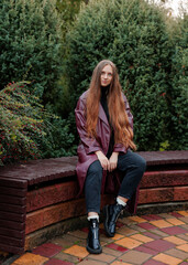 Woman with long hair wearing stylish coat sitting on bench outdoors