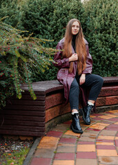 Woman with long hair in maroon coat sitting on bench in park setting