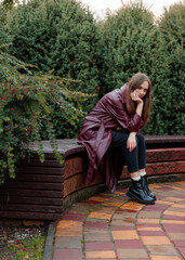 Young woman in maroon coat sitting on stone bench in garden setting