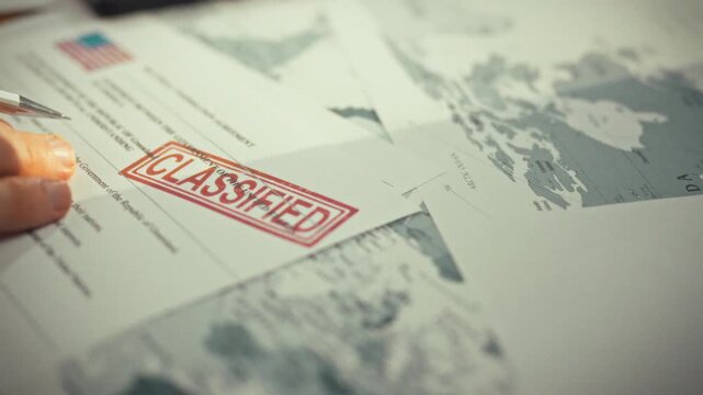 A person's hands grasp a pen while scrutinizing an official administration document stamped with a high-security clearance on a table surrounded by maps and departmental papers