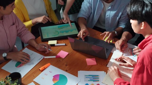 Top view of team discussing and analyzing financial chart while pointing at tablet. Diverse business team brainstorming and planning strategy while using stock market chart and laptop. Convocation.