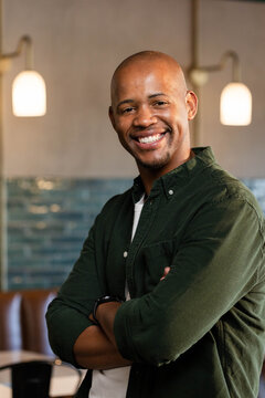 African American man smiling with crossed arms in cafe wearing button shirt, pendant lamps visible