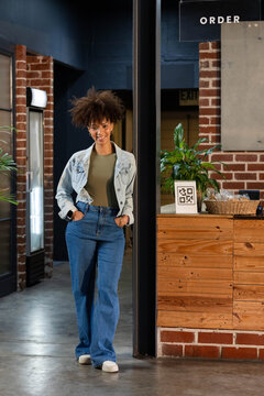 African American woman leaning on black metal post inside cafe near wooden counter with QR code