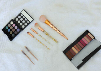 Fototapeta premium Rose-gold powder brush and gold-flake brushes are resting on white towel with palettes