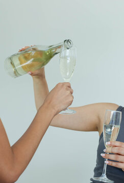 Manicured hands are pouring pale sparkling wine into flute against pale gray wall, with bubbles