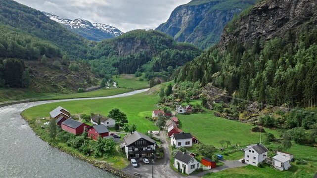 Aerial view of green valley and farmland near Flam village in Norway. Drone footage shows scattered houses, winding river and dramatic mountain landscape.
