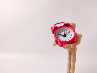 Small, red, retro-style analog alarm clock held by a wooden articulated mannequin