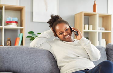 African American woman enjoying leisure time at home, using a smartphone to make a phone call. She...