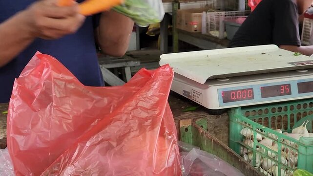 Market vendor weighing produce and packing vegetables in plastic bag. Grocery stall scale checkout with seller bagging fresh food items. Traditional marketplace transaction using digital scale and pac