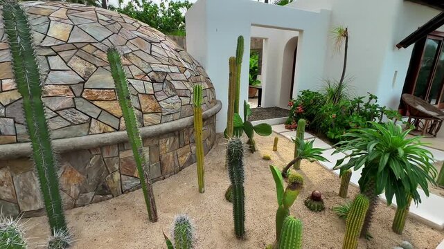 Traditional Mexican villa courtyard featuring a stone temazcal dome surrounded by cacti and tropical plants, blending indigenous architecture with luxury resort design.