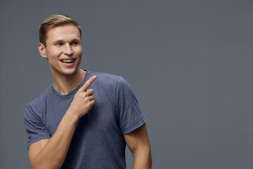 Smiling man with short brown hair wearing casual blue t-shirt, pointing upward with his right hand,...