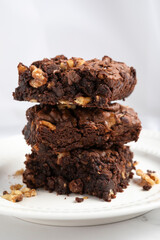 A close-up of rich, fudgy chocolate brownies stacked on a white plate, filled with crunchy walnuts and baked to a moist, homemade texture. Shot on a clean, minimalist background with soft natural ligh
