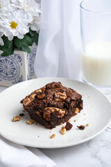 A close-up of rich, fudgy chocolate brownies stacked on a white plate, filled with crunchy walnuts and baked to a moist, homemade texture. Shot on a clean, minimalist background with soft natural ligh