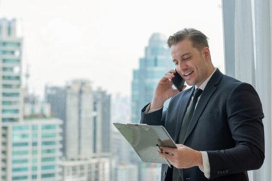 businessman manager man in suit talking phone looking clipboard. business communication successful entrepreneur phone conversation confident urban professional executive lifestyle on smartphone - Powered by Adobe