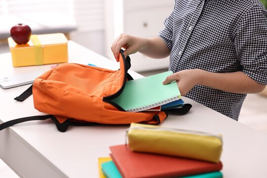 Boy packing his backpack for school at desk indoors, closeup