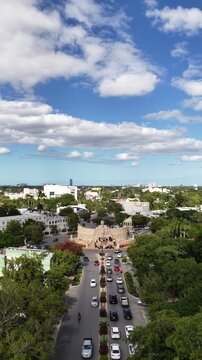 Aerial drone flying forward towards Monumento a la Patria roundabout with traffic and cloudy blue sky in M&eacute;rida, Yucat&aacute;n. Vertical video