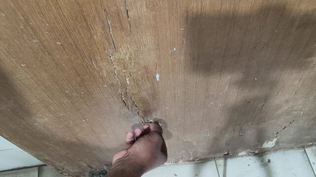 A damaged wooden door. A large, jagged hole reveals the crumbly, white texture inside, indicating termite infestation. The surrounding wood is light brown, while the interior is hollow and rotten.