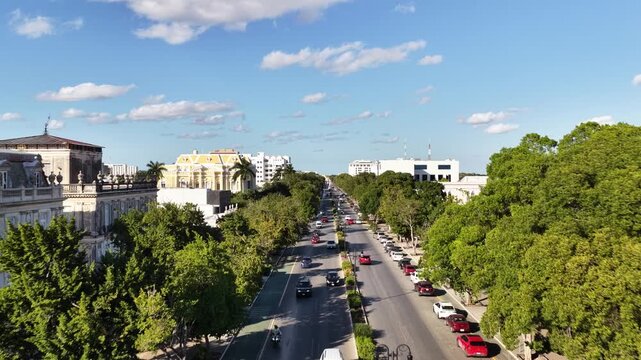 Aerial drone flying forward and ascending over Paseo Montejo with colonial mansions, city skyline and clouds in M&eacute;rida, M&eacute;xico