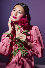 Young woman in pink elegant long sleeve dress holds bright red peony flower. She gently touches her...