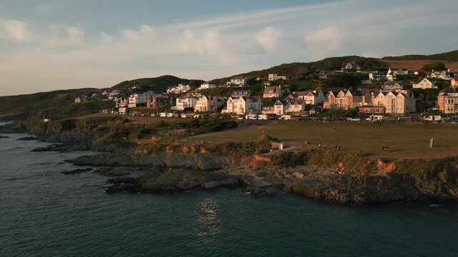 Coastal town with white houses on a hill overlooking a rocky shoreline and calm ocean at sunset.