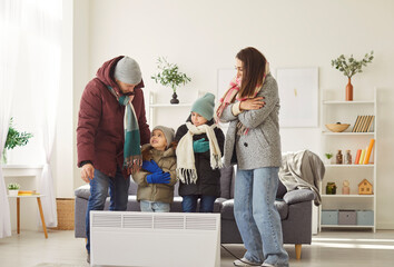 Family with children try to stays warm near an electric heater at home during cold weather or...