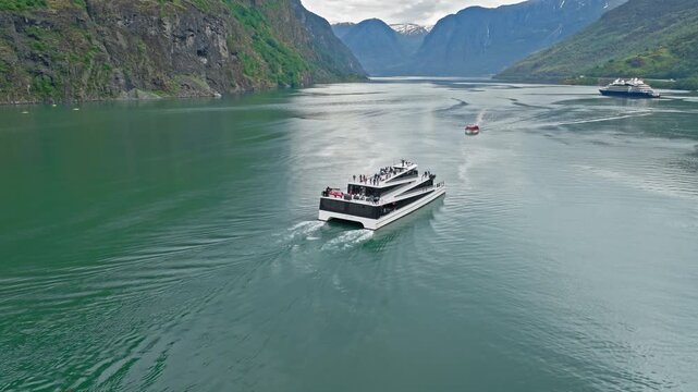 Aerial view of a ferry boat cruising through the Norwegian fjord near Fl&aring;m. Calm green water and steep mountains showcase peaceful Norway transportation and travel.