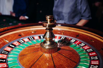 Casino table with roulette wheel in motion, with casino chips, tokens, the hand of croupier, dollar money and a group of gambling rich people playing bet on a party, blue poker table and deck of cards