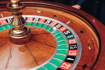 Casino table with roulette wheel in motion, with casino chips, tokens, the hand of croupier, dollar money and a group of gambling rich people playing bet on a party, blue poker table and deck of cards