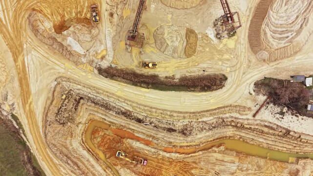 Heavy machinery operates on a construction and mining site. Trucks and excavators move dirt and rocks. Land is being reshaped and prepared for future development.