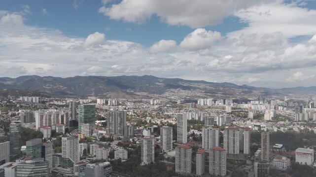 erial panoramic view of the Santa Fe district in Mexico City as the drone moves laterally over residential towers with mountains and a dramatic cloudy sky in the background.