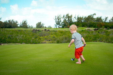 Obraz premium Barefoot Toddler Runs Across Golf Fairway With Club, Tropical Vacation