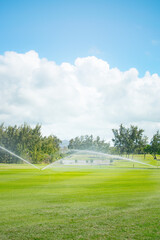 Fototapeta premium Automated irrigation on lush golf course green under sunny sky.