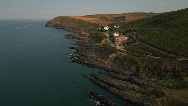 Coastal village nestled among green hills overlooking a rugged shoreline and the ocean. Farms dot the landscape.