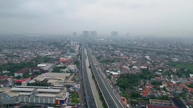 Aerial view of a modern highway cutting through dense housing, showing urban growth, transport flow, and city infrastructure in daylight.