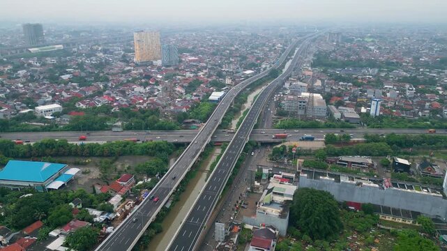 Aerial view of busy toll road crossing dense city area with bridges, cars, and urban housing, showing transport flow and city growth.