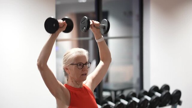 Mature woman exercises in gym while lifting weights to improve her strength and overall fitness during evening workout.