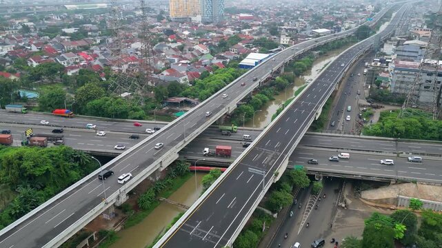 Aerial view of busy toll road crossing dense city area with bridges, cars, and urban housing, showing transport flow and city growth.