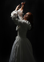 Fototapeta premium close up portrait beautiful female model wearing antique white historical ghost bride wedding dress gown. Overhead silhouette lighting, dark studio background. looking up towards light, hands reaching