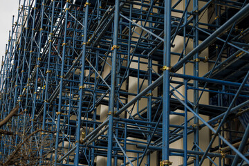 Complex network of blue metal scaffolding is set up against building under construction, showcasing intricate framework essential for supporting workers and materials