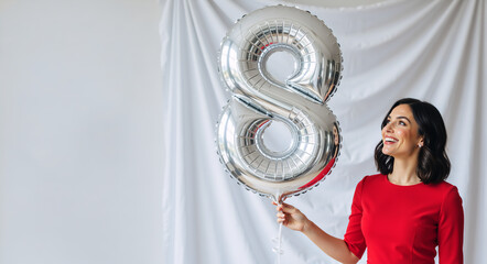 Happy woman holding silver balloon number 8. Smiling female in red dress celebrating eighth birthday or anniversary. International Women's Day concept with copy space
