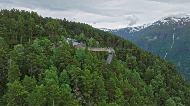 Aerial view of Stegastein viewpoint surrounded by dense forest above Aurlandsfjord, Norway. Mountain platform and winding road sit high above the fjord in a dramatic landscape.