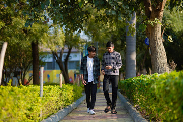 Obraz premium two indian teenagers boys looking smartphone and discussing at garden
