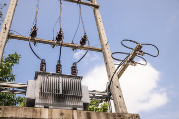 Power transformer and high voltage cables mounted on concrete utility structure in tropical Thailand, clear blue sky and green trees in background