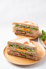 Whole wheat bread sandwich with bacon, lettuce, tomato and fried egg on wooden plate