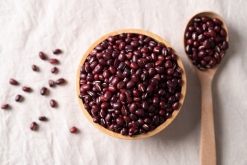 Top view of Azuki beans, Adzuki bean or red mung beans in wooden bowl and spoon on white fabric background, Food ingredients in many Chinese dishes and filling in Japanese sweet
