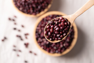 Top view of Azuki beans, Adzuki bean or red mung beans in wooden spoon and bowl on white fabric background, Food ingredients in many Chinese dishes and filling in Japanese sweet