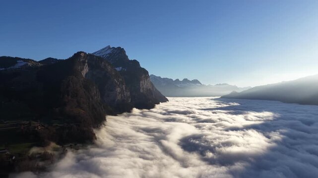 Breathtaking morning sea of clouds flowing through the valley below steep cliffs near Lake Walensee in the Swiss Alps.