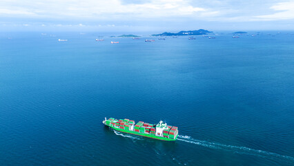 a green cargo container ship sailing in a vast blue ocean. The horizon features a busy shipping...